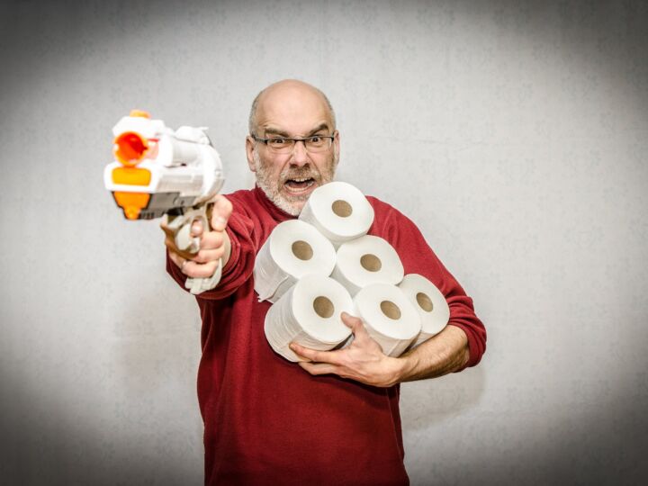 Mann mit Plastikpistole, seine WC-Rollen verteidigend