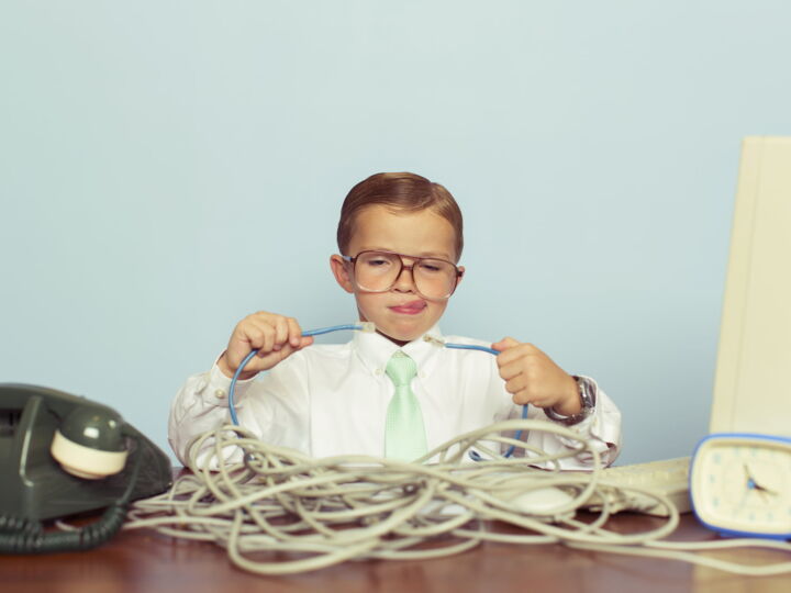 A young IT professional working with a large pile of tangled internet cables on his desk. He is dressed in a white shirt, tie and glasses while trying to reconnect his broken network. Retro styling. This IT technician can solve any network problem.