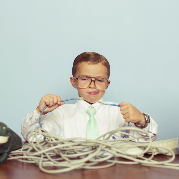 A young IT professional working with a large pile of tangled internet cables on his desk. He is dressed in a white shirt, tie and glasses while trying to reconnect his broken network. Retro styling. This IT technician can solve any network problem.